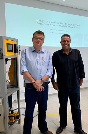 Vladimir Kuse, Diretor da Automasafety ao lado de Ricardo Lecke, Engenheiro Mecânico. Eles estão em uma sala com um telão. No lado esquerdo tem uma máquina com uma pequena tela e um aparelho com vários botões. O engenheiro usa óculos de grau e relógio. Os dois estão com camisa social: mangas compridas, botões e gola.
