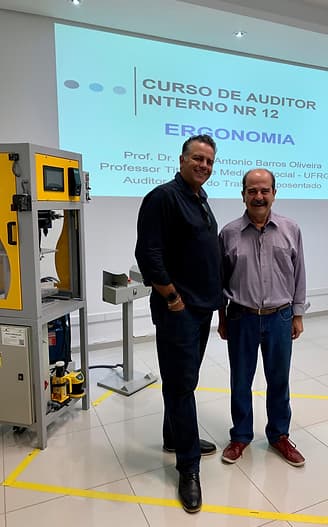 Vladimir Kuse, Diretor da Automasafety ao lado do Doutor Paulo Antônio Barros, Especialista em medicina do trabalho. Atrás deles há um telão com informações escritas,  a palavra visível é Ergonomia. Os dois homens estão em pé sorrindo, eles usam camisa social de mangas compridas, botões e gola.