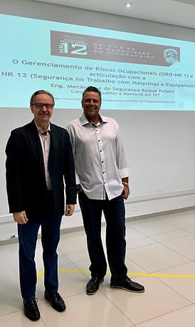 Vladimir Kuse, Diretor da Automasafety ao lado de Roque Puiatti, Engenheiro Mecânico e de Segurança do Trabalho. Eles estão em uma sala sorrindo. Os dois usam camisa social de mangas compridas, botões e gola, a diferença é que o Engenheiro está com uma terceira peça, um blazer.